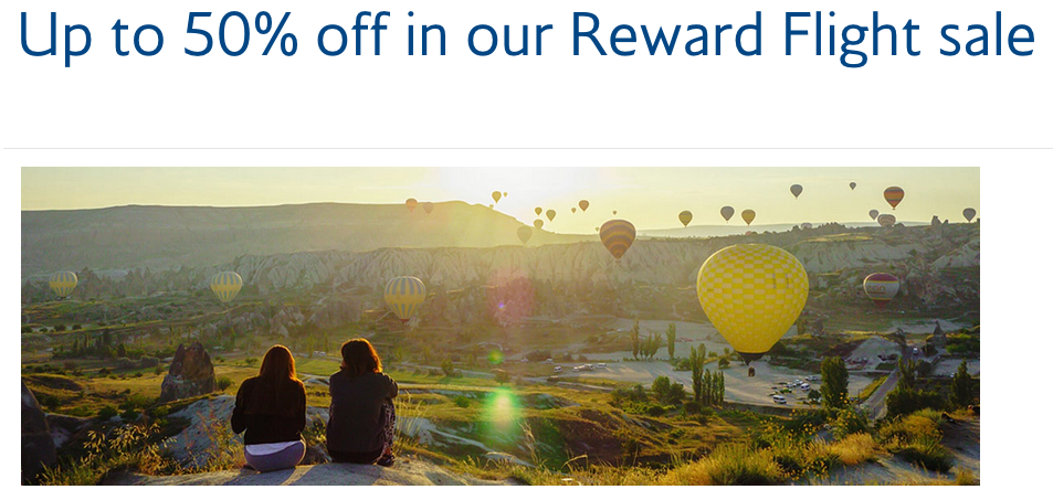 a group of people sitting on a hill looking at hot air balloons